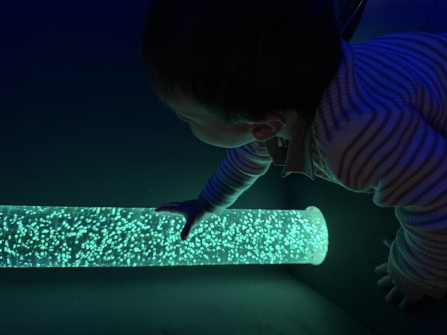 A child exploring a glowing sensory bubble tube in the sensory room